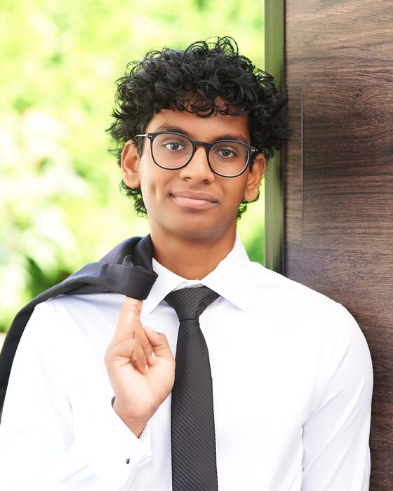 Ankit Karthik, founder of TechBridge, smiling in a white shirt and black tie with a jacket over his shoulder